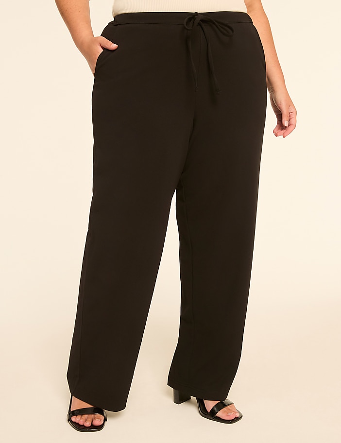 A person stands in black wide-leg pants with a drawstring waist and open-toe heels against a plain, light-colored background.