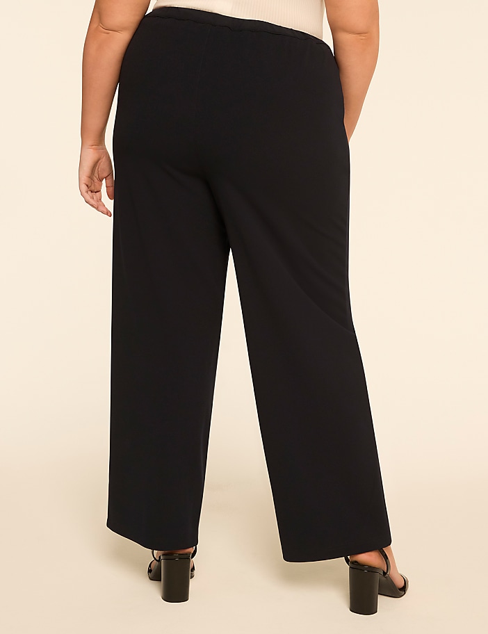 A person wearing black wide-leg pants and black heels stands against a plain beige background.
