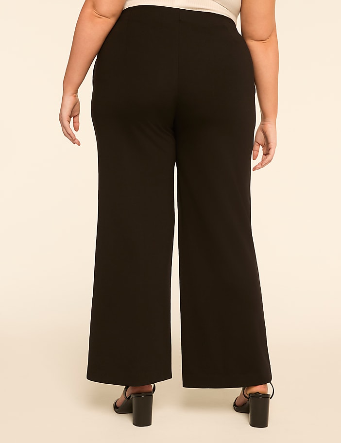 A person wearing black wide-leg pants and black heels stands against a plain, light-colored background.