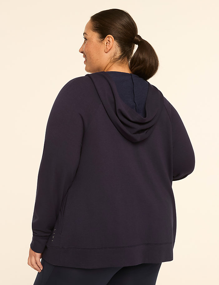 A woman in a navy hoodie stands against a plain, light-colored background.