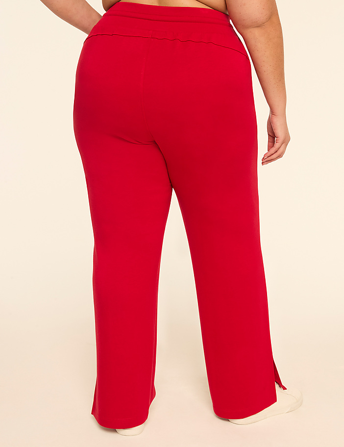 A person wearing red pants with a slit at the hem stands against a plain beige background.
