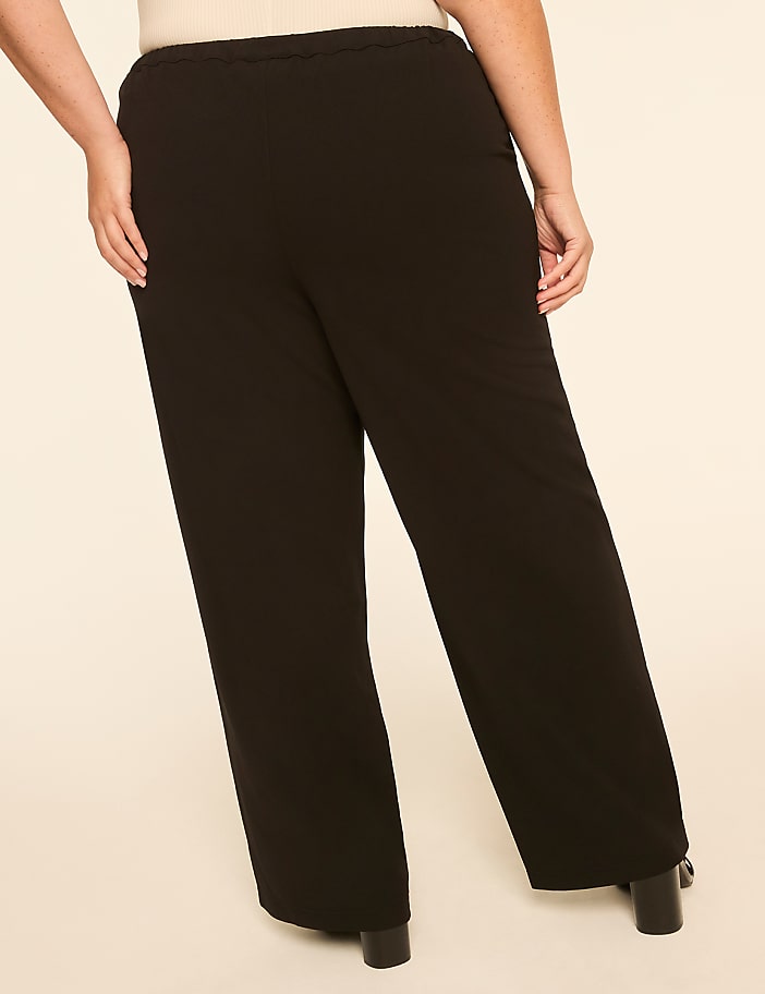 A person wearing black wide-leg pants stands against a plain, light-colored background.