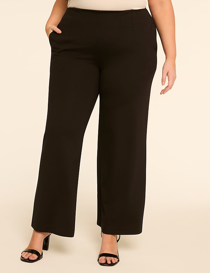 A person wearing black wide-leg pants and black heels stands against a plain, light-colored background.