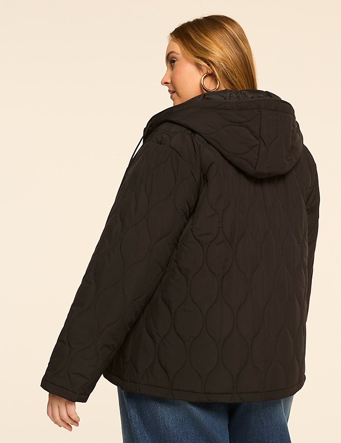 A woman in a black quilted jacket stands against a plain, light-colored background.
