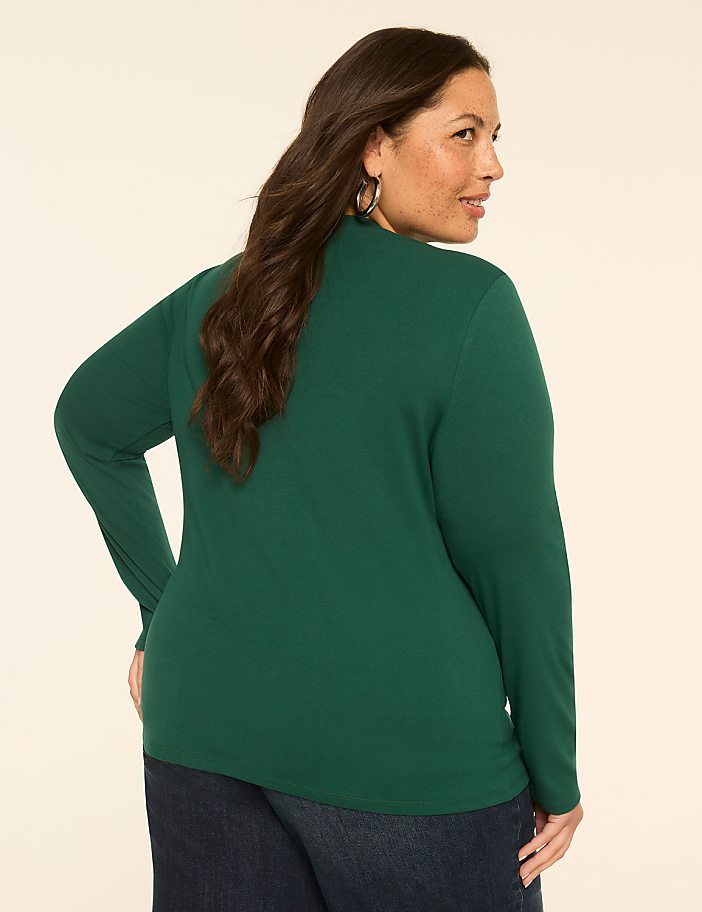 A woman in a green turtleneck and jeans stands against a plain, light-colored background.