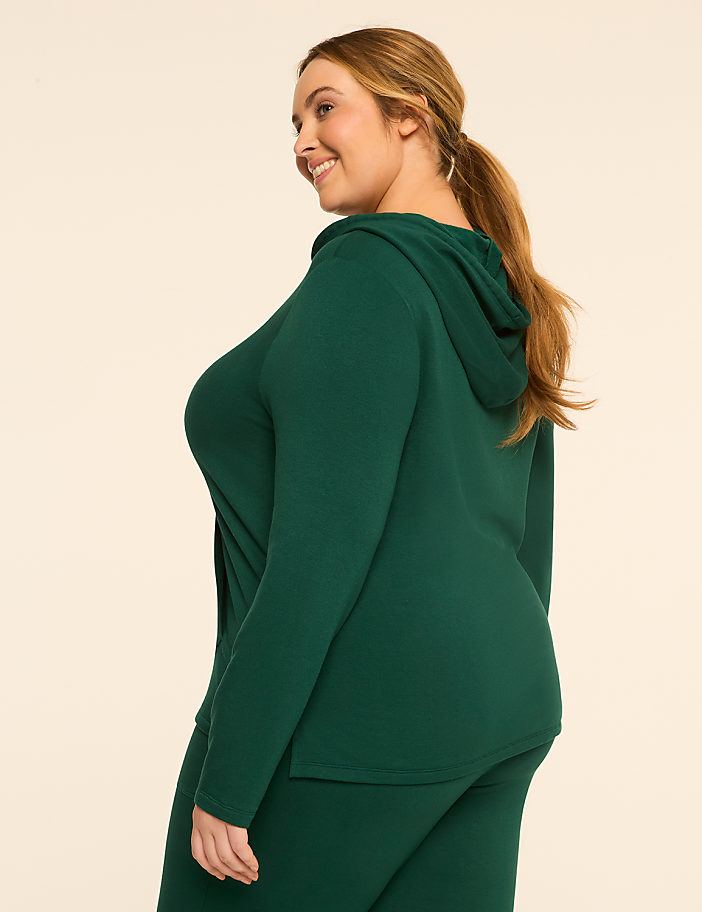 A woman in a green hooded top and pants stands against a plain, light-colored background.