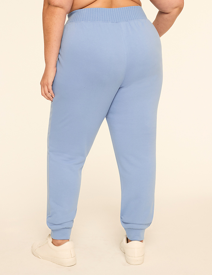 A person wearing light blue sweatpants and white sneakers stands against a plain, light-colored background.