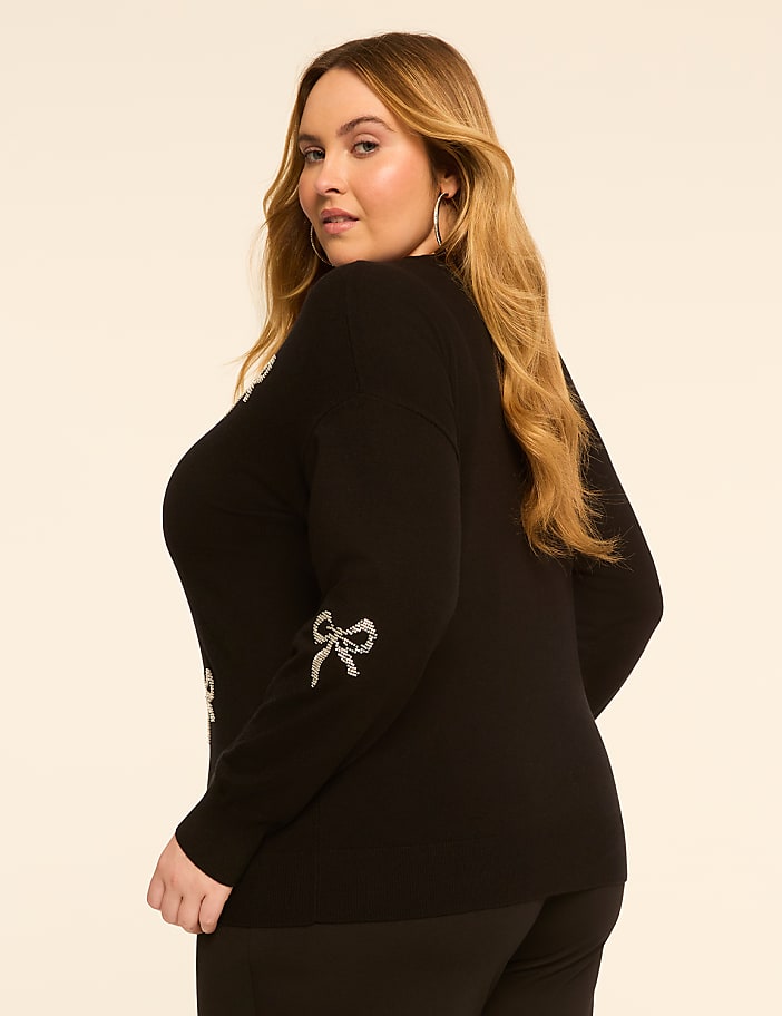 A woman in a black sweater with sequined bows stands against a plain, light-colored background.