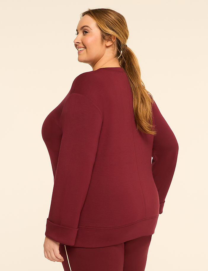 A woman in a maroon sweatshirt and pants stands against a plain, light-colored background.