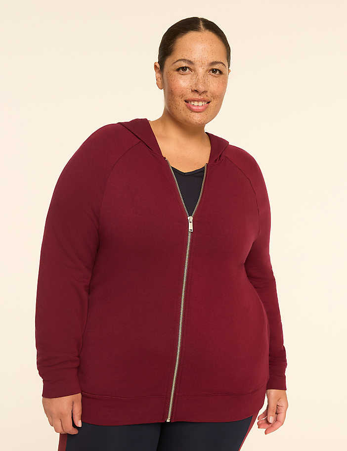 A woman in a maroon zip-up hoodie stands against a plain, light-colored background.