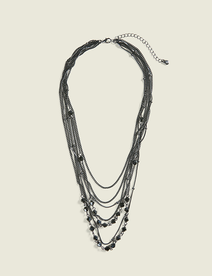 A layered, dark metal necklace with black beads rests against a plain, light beige background.
