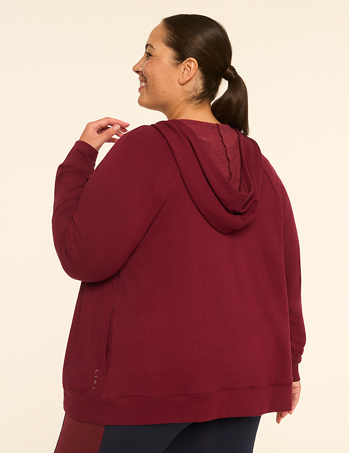 A woman in a maroon hoodie stands against a plain, light-colored background.