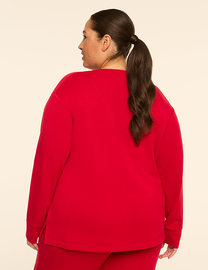 A woman in a red sweater and pants stands against a plain, light-colored background.