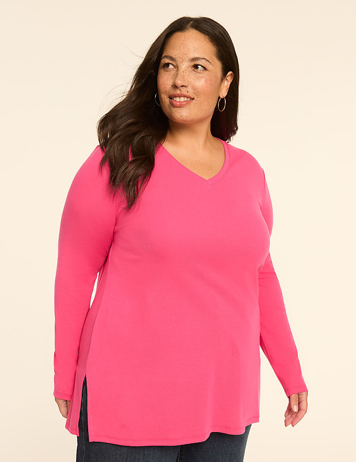 A woman in a bright pink v-neck shirt stands against a plain, light-colored background.