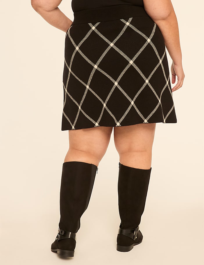 A person wearing a black and white plaid skirt and black boots stands against a plain, light-colored background.