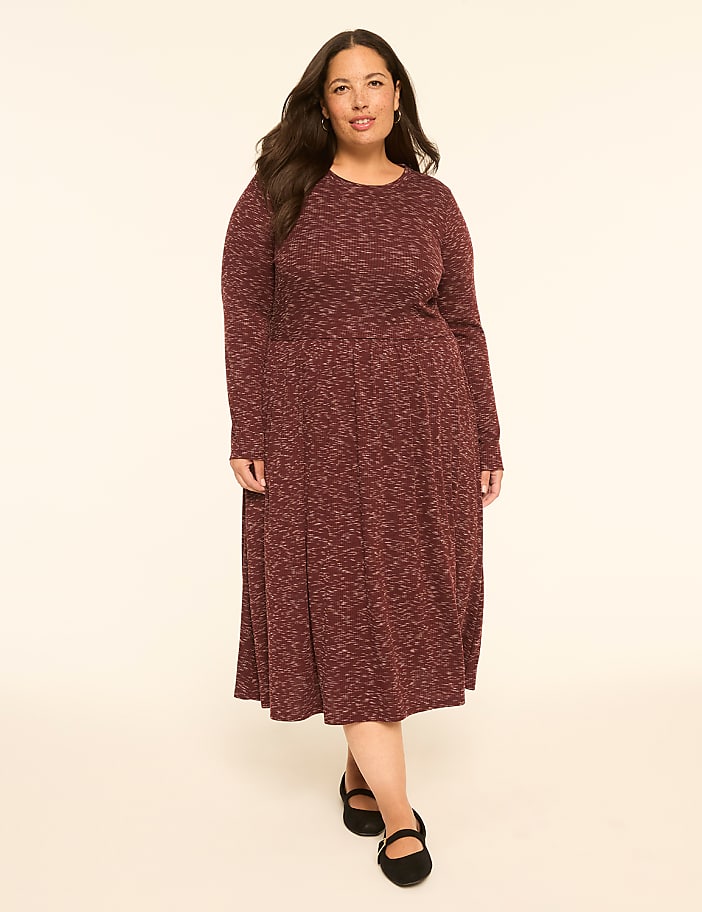 A woman in a maroon marled knit dress and black flats stands against a plain, light-colored background.