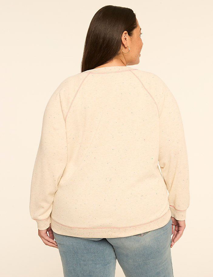 A woman in a cream-colored sweatshirt and jeans stands against a plain, light-colored background.
