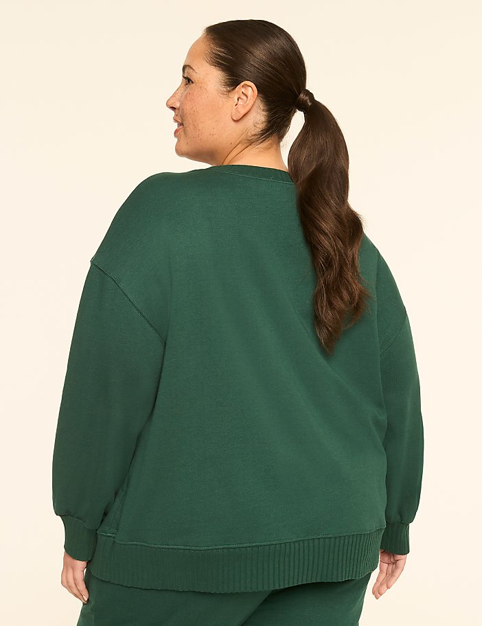 A woman in a green sweatshirt stands against a plain, light-colored background.