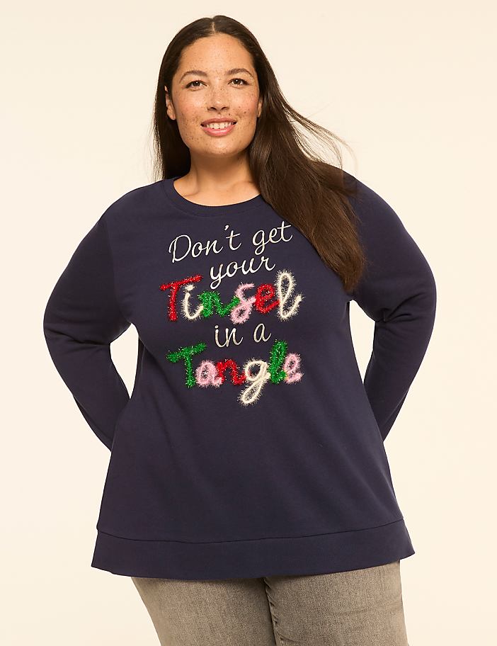 A woman in a navy blue sweatshirt with a festive holiday slogan stands against a plain, light-colored background.