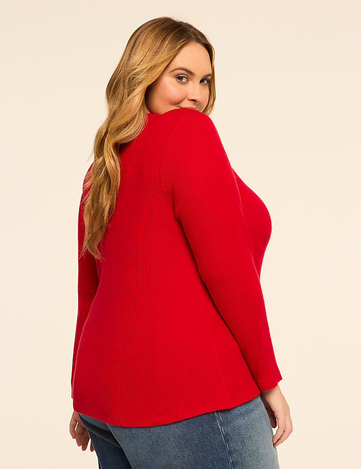 A woman in a red top and blue jeans poses against a plain, light-colored background.
