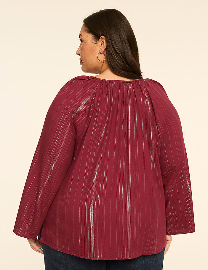 A woman in a maroon striped blouse stands against a plain beige background.