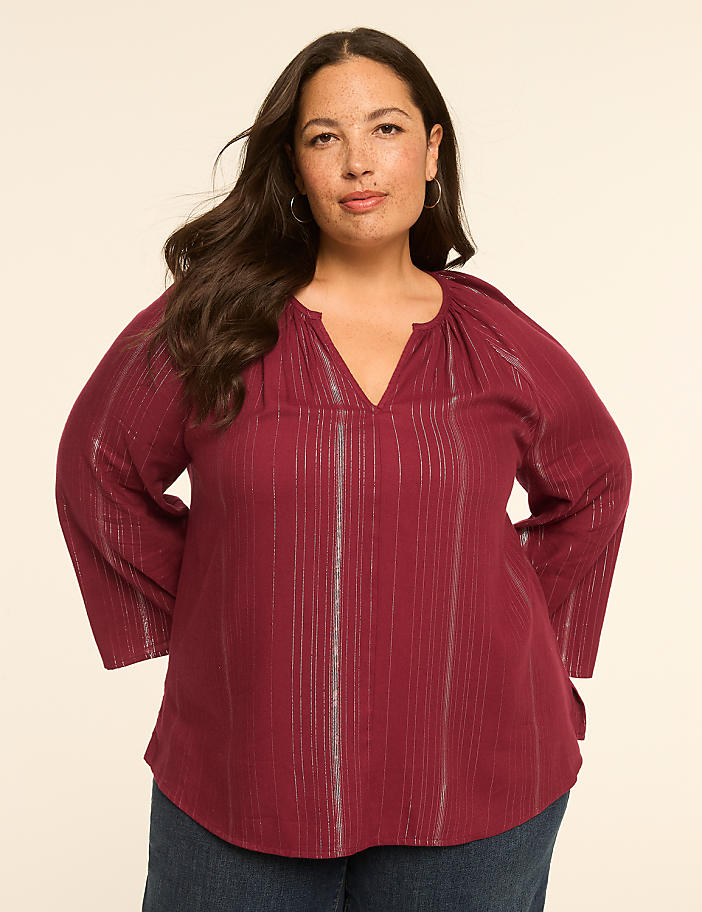 A woman in a burgundy striped top stands against a plain, light-colored background.
