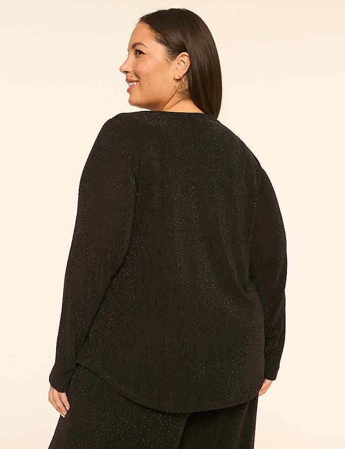 A woman in a black sparkly top and pants stands against a plain, light-colored background.