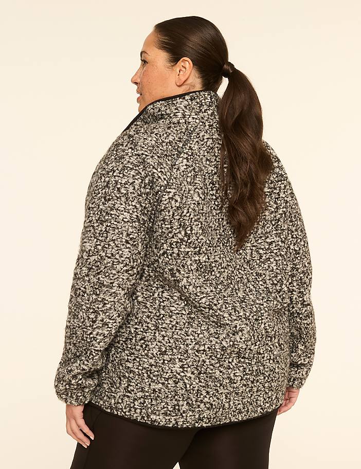 A woman in a speckled gray jacket stands against a plain, light-colored background.