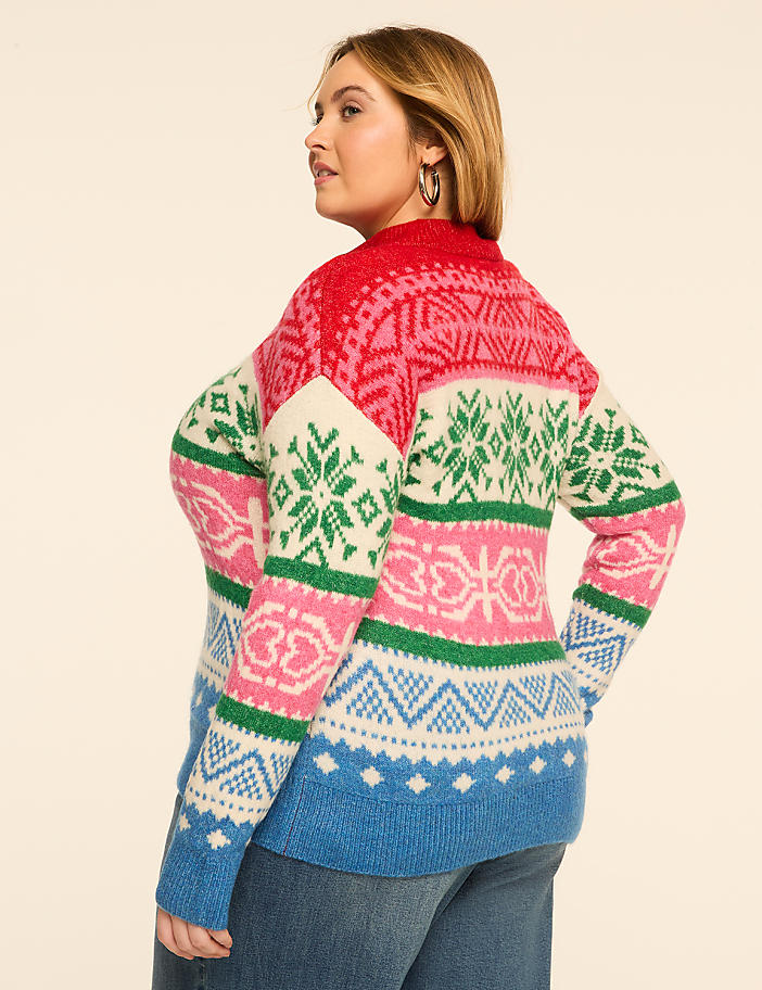 A woman in a colorful, patterned sweater stands against a plain, light-colored background.