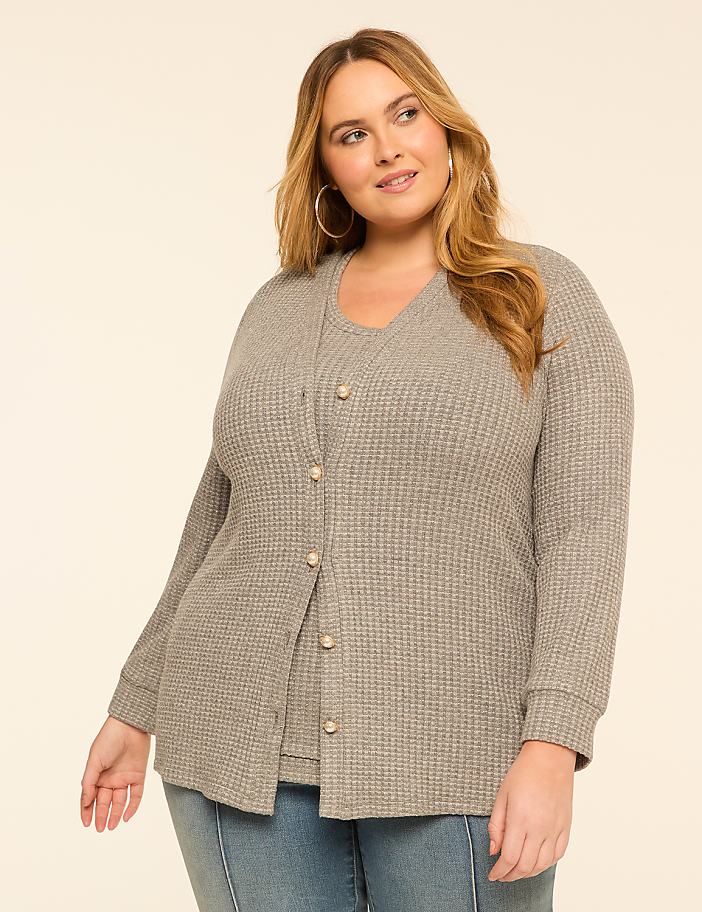 A woman in a grey waffle-knit cardigan and camisole stands against a plain, light-colored background.