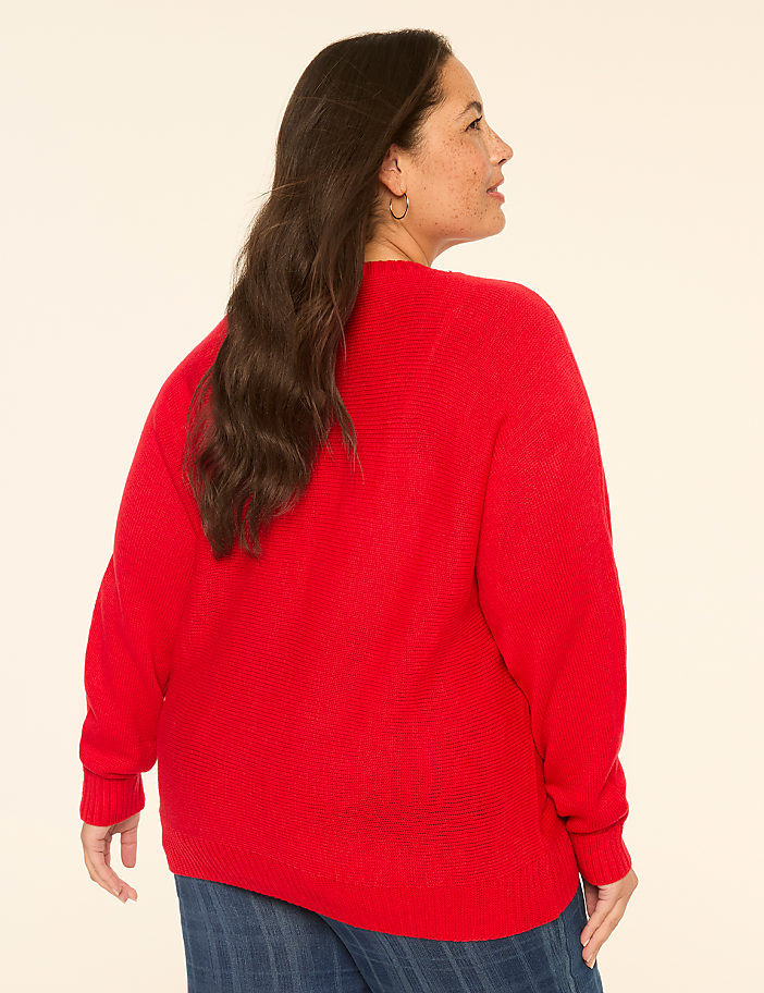 A woman in a red sweater stands against a plain, light-colored background.