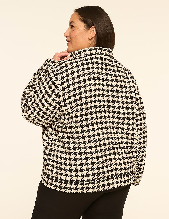 A woman in a black and white houndstooth jacket stands against a plain, light-colored background.