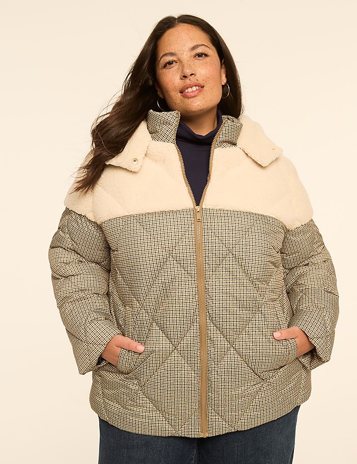 A woman in a cream and plaid puffer jacket stands against a plain, light-colored background.