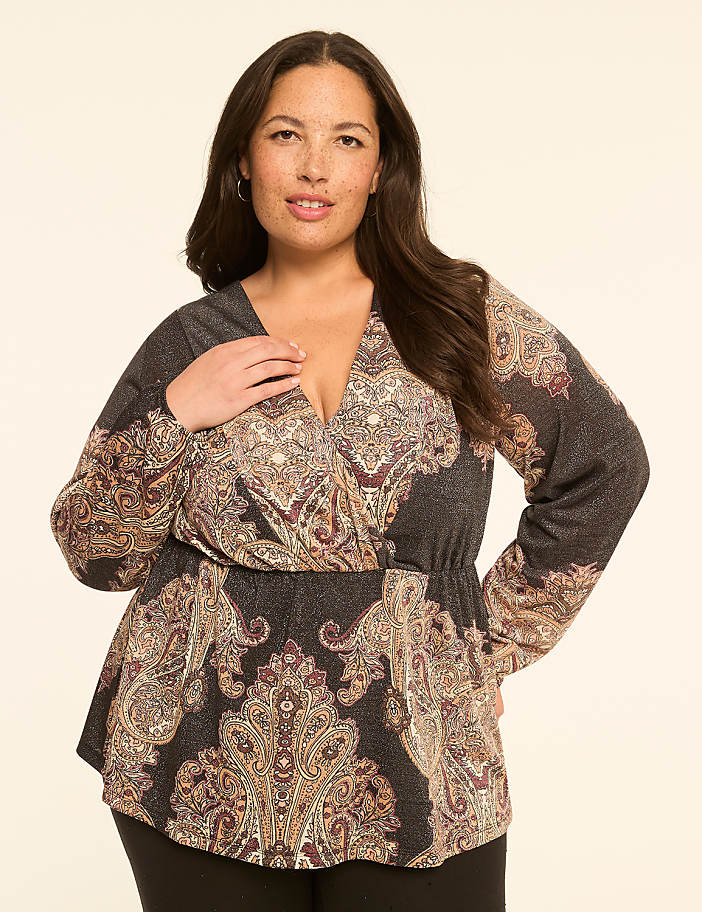 A woman in a patterned wrap top stands against a plain, light-colored background.
