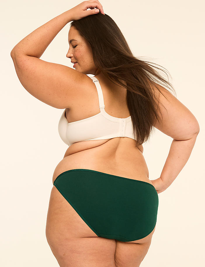 A woman in a white bra and green underwear poses against a plain, light-colored background.