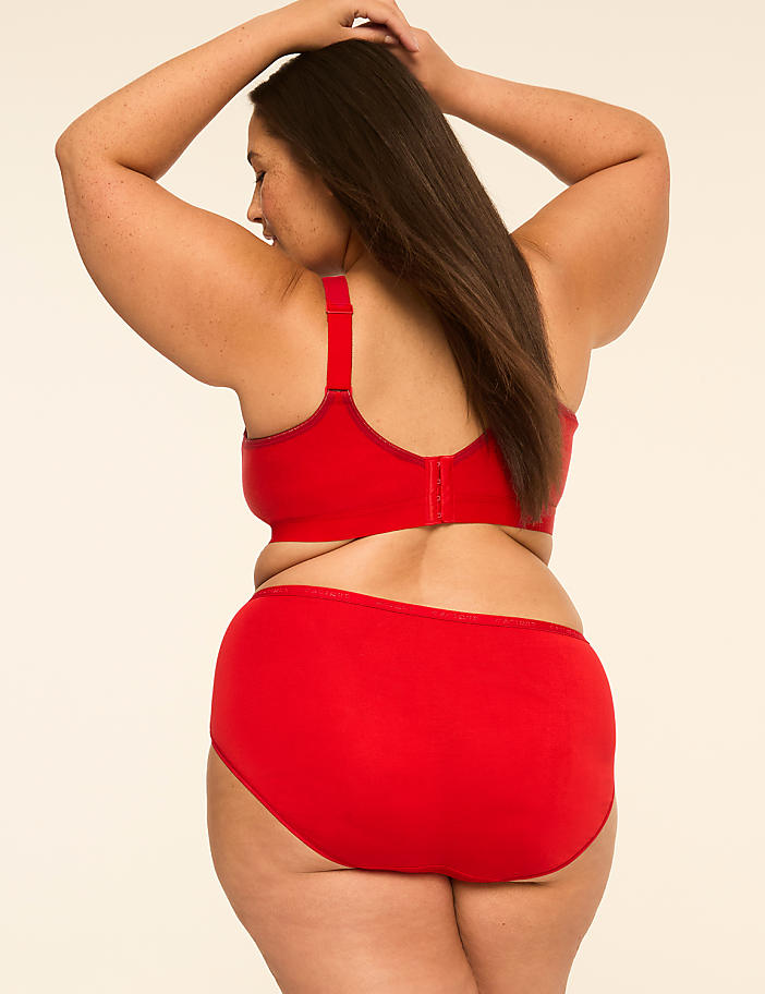 A woman in a red bra and panties stands with her back to the viewer, arms raised, against a plain, light-colored background.