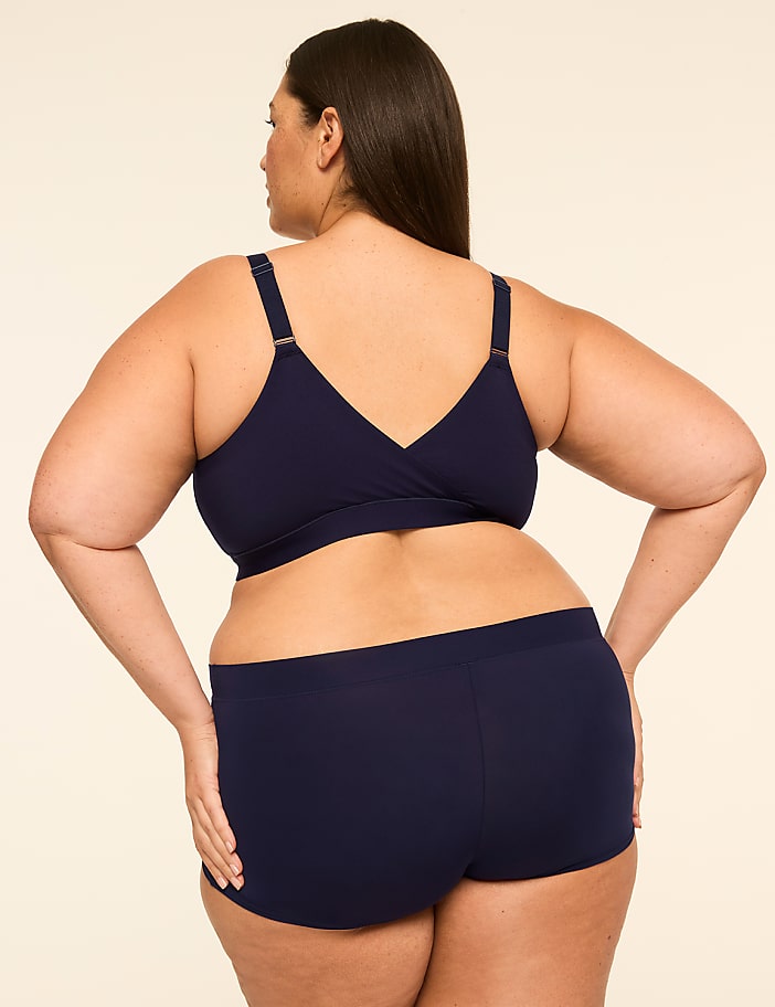 A woman in navy blue undergarments stands with her back to the viewer against a plain, light-colored background.