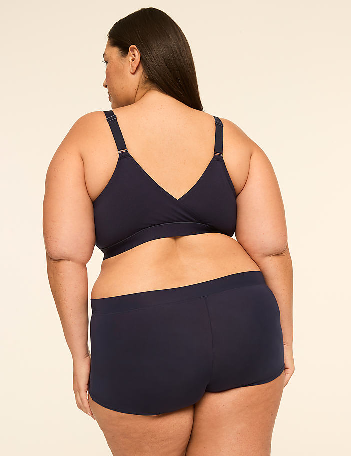 A woman in navy blue lingerie stands against a plain, light-colored background.