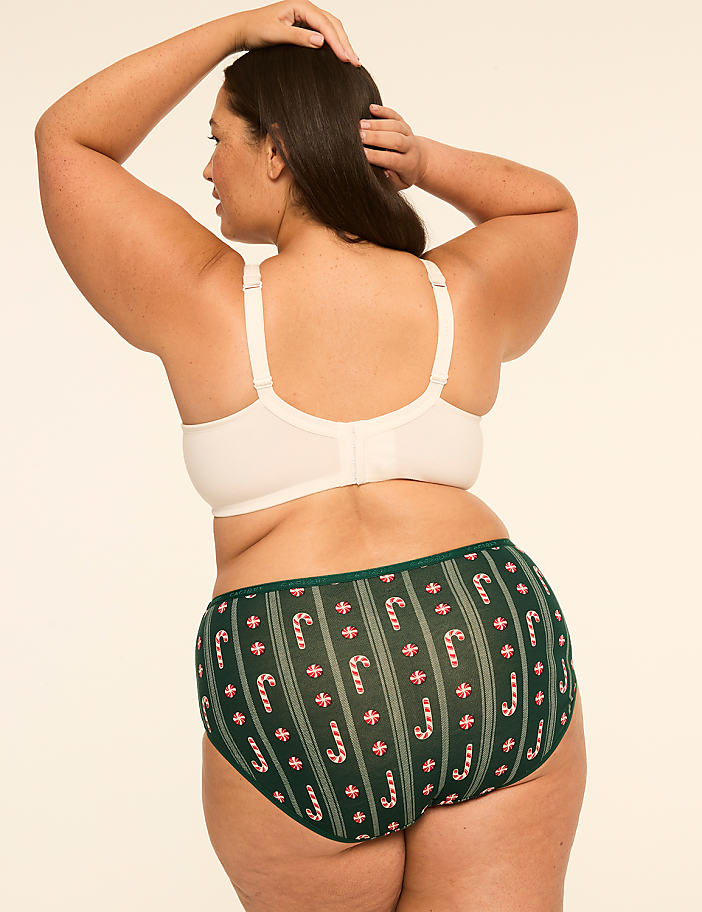 A woman in a cream-colored bra and green candy cane patterned underwear stands against a plain, light background.