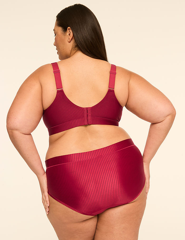A woman in a burgundy ribbed bra and matching high-waisted briefs stands against a plain, light-colored background.