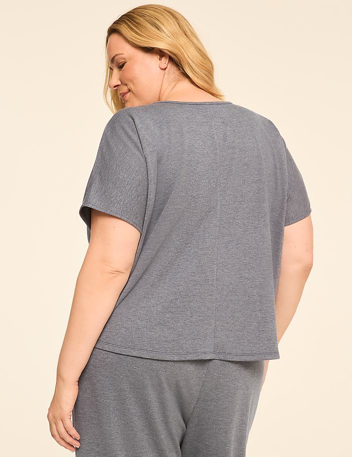 A woman in a grey top and pants stands against a plain cream background.