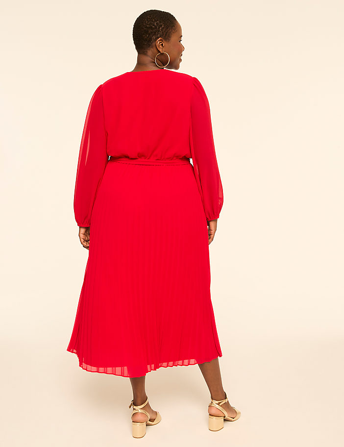 A woman in a red dress stands against a plain, light-colored background.