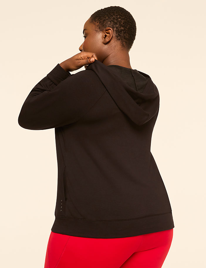 A woman in a black hoodie and red leggings stands against a plain, light-colored background.