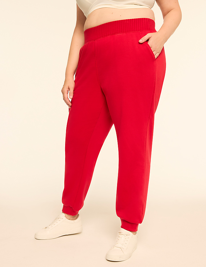 A person in red sweatpants and white sneakers stands against a plain, light-colored background.
