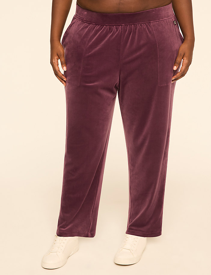 A person wearing plum-colored velour pants and white sneakers stands against a plain, light-colored background.