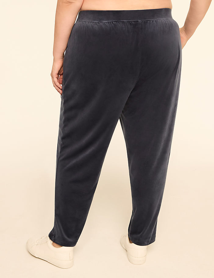 A person wearing dark blue velvet pants and white sneakers stands against a plain, light-colored background.