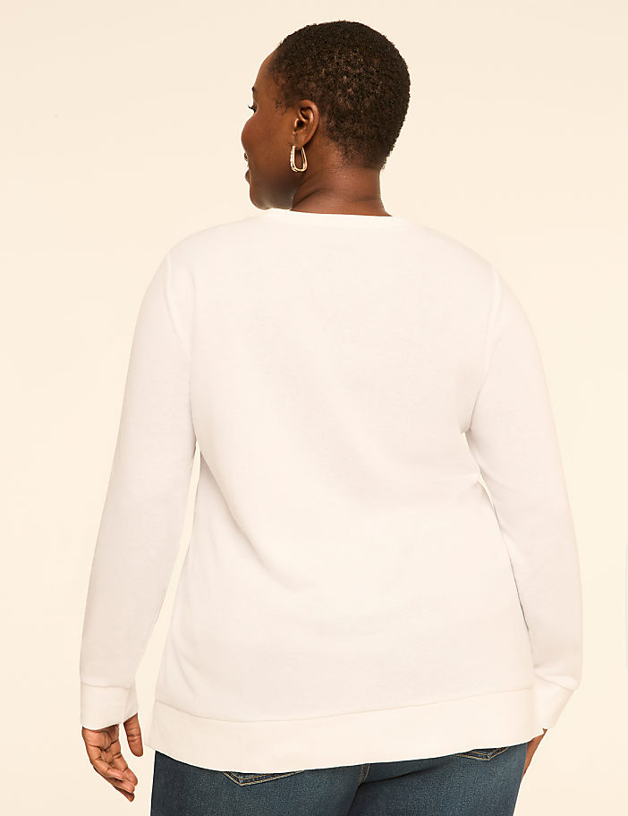 A woman in a white long-sleeved shirt and blue jeans stands against a plain, light-colored background.