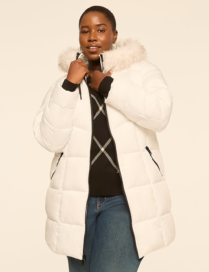 A woman in a white puffer coat with a fur-lined hood stands against a plain, light-colored background.