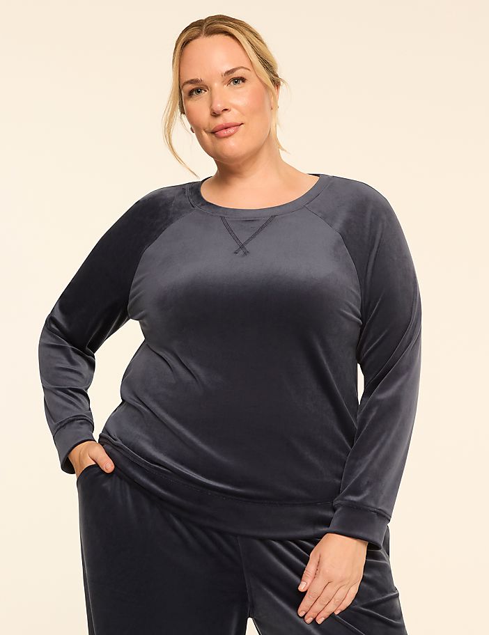 A woman in a gray velvet sweatshirt and pants stands against a plain, light-colored background.