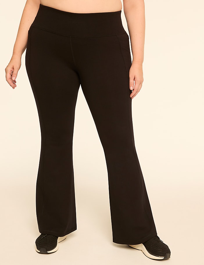 A person wearing black flare yoga pants and sneakers stands against a plain, light-colored background.